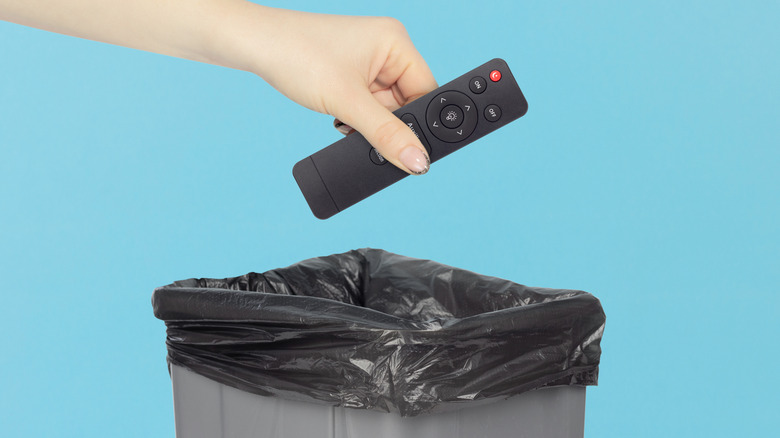a person's hand throwing a TV remote into a trashcan