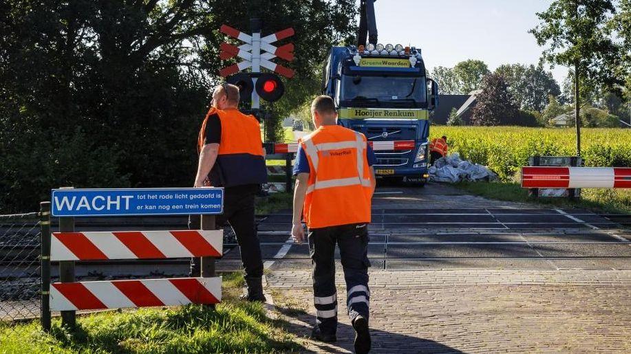 Rail workers in hi vis jackets are pictured at a level crossing in Holten in the Netherlands on Tuesday. In the background a lorry can be seen parked on the other side of the crossing, while another worker is seen next to a large pile of building sacks.