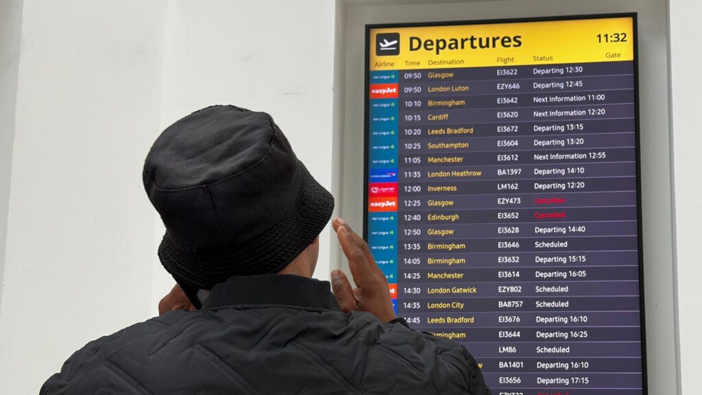 Woman stands in front of board showing two cancelled flights and others departing late