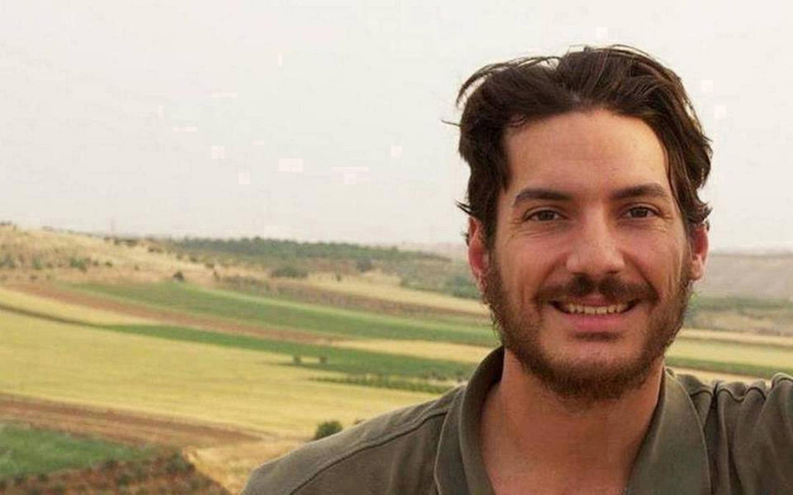 File image of Tice in front of a rural background. He has mid-length brown hair and a short brown beard and is wearing a khaki green polo shirt.
