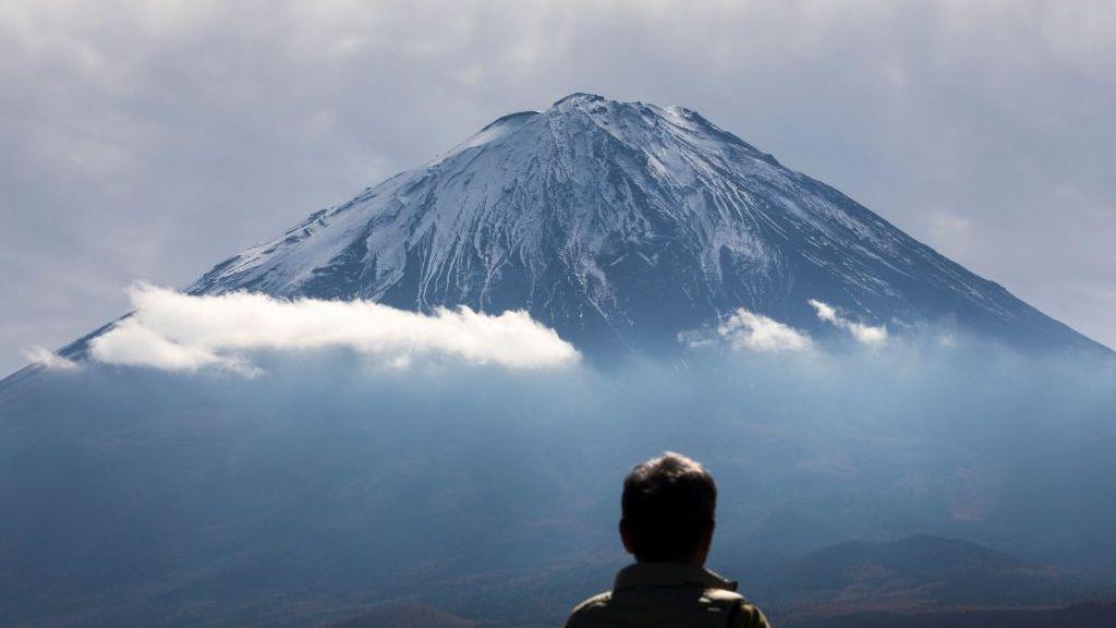 The snow-capped summit of Mount Fuji in Japan with the head of a man in the foreground