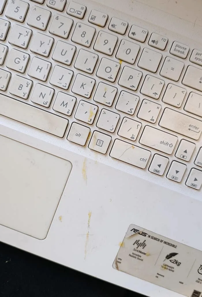 A laptop keyboard with visible wear and food stains on the keys and area near the touchpad