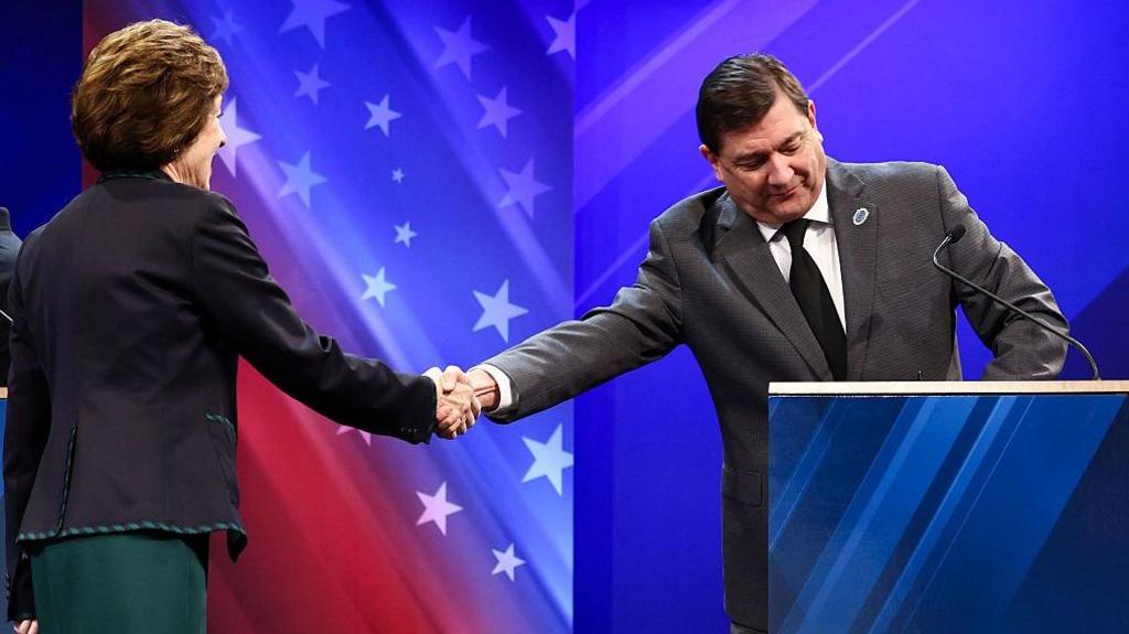 Collins in black jacket and green skirt, Jackson in grey suit and black tie, background of red and blue with white stars