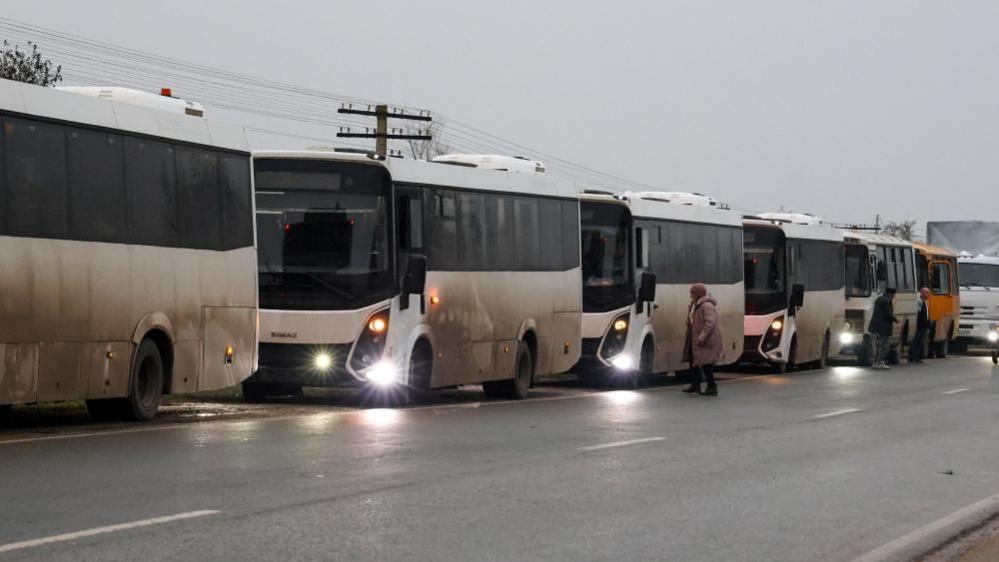 A row of white coaches are parked up on the side of the road