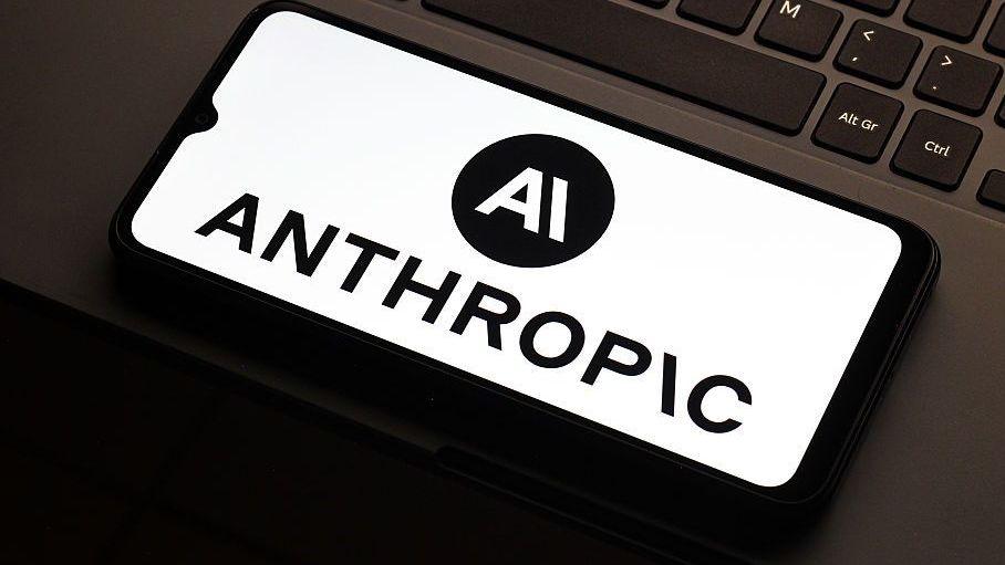 Anthropic logo on a smarthphone which is lying flat on the mousepad of a laptop. Only a partial keyboard of the laptop is visible.