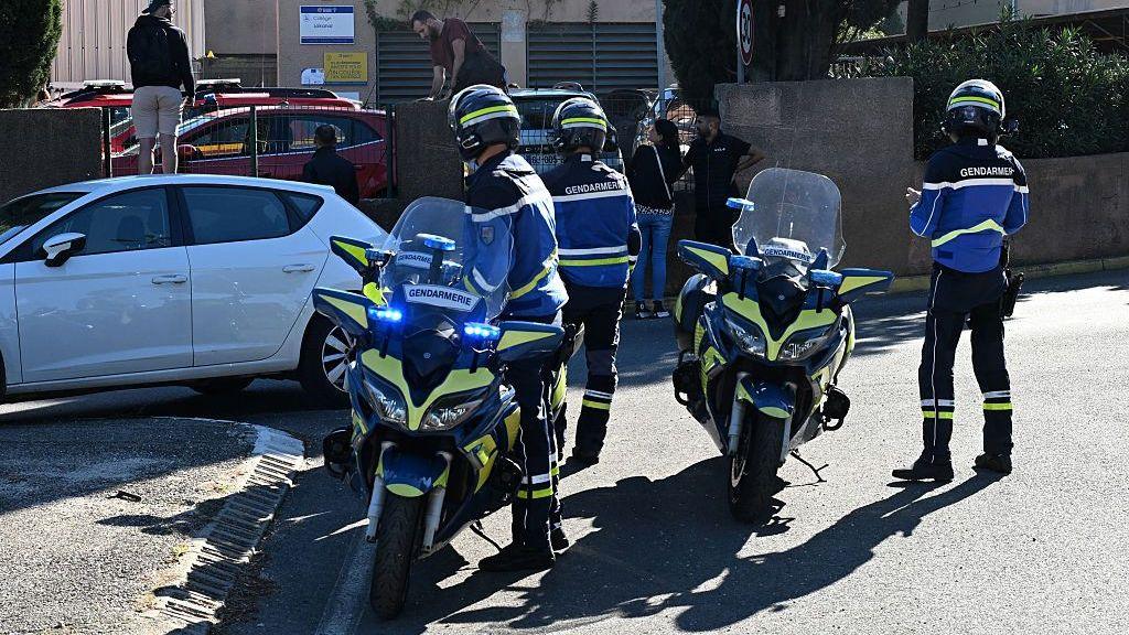 Three French police officers in uniform arrive at Lakanal school on motorbikes.