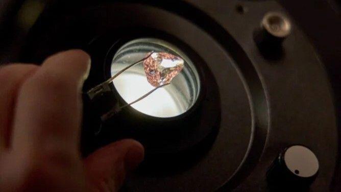A person inspects the backlit Grand Condé diamond under a microscope.