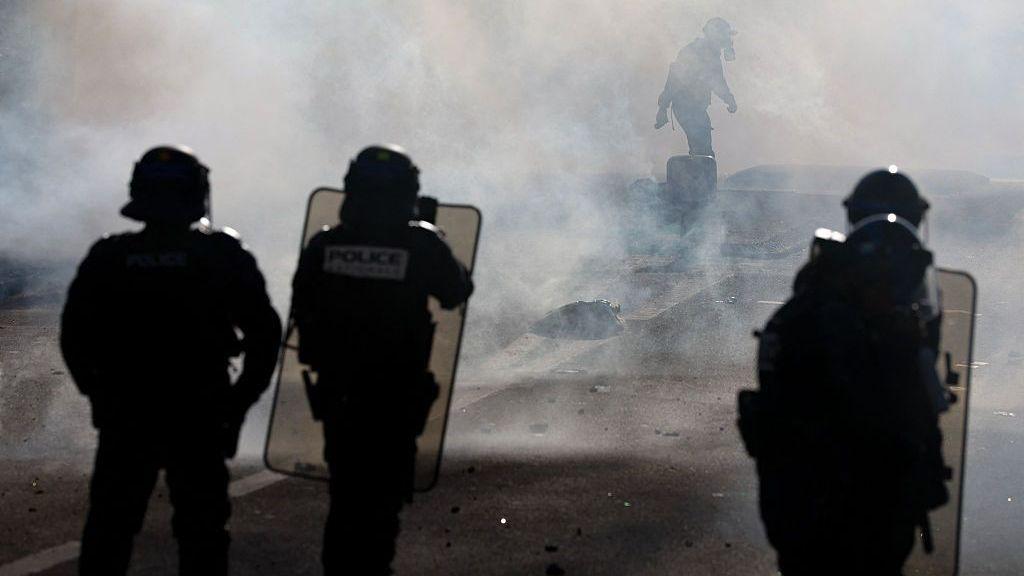 Four riot police, all wearing helmets and two carrying large shields, can be seen surrounded by smoke during a protest in Brest on 1 October