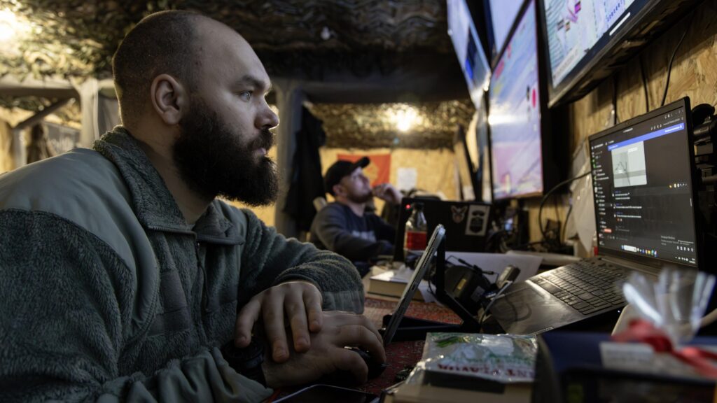A close up of a Ukranian soldier surrounded by computer screens