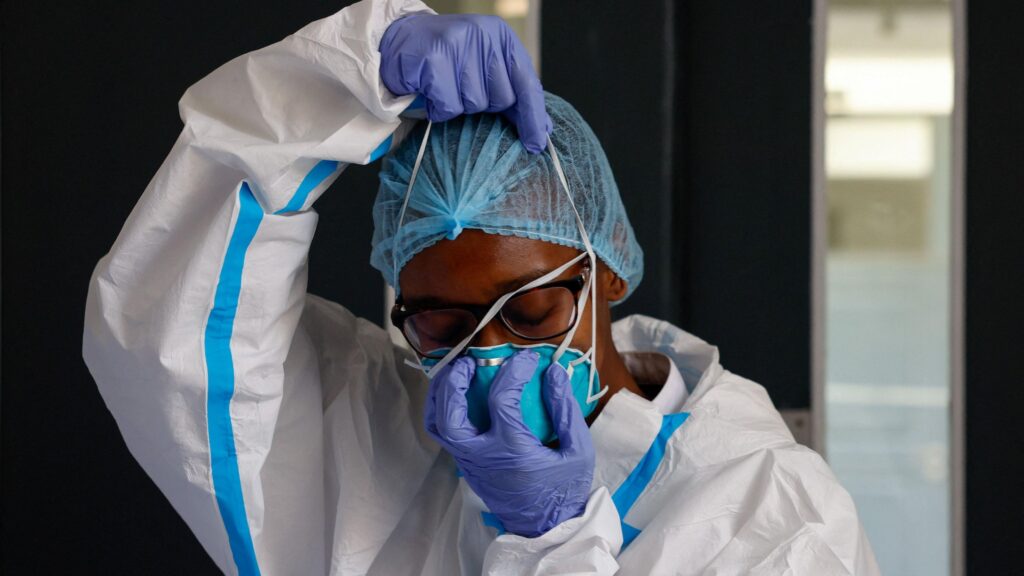 A nurse wears in white protective clothes and blue gloves, wears a face mask