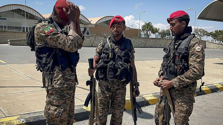 Three members of the Ethiopian National Defense Force (ENDF) in military fatigues and red berets. Behind them is the Mekelle Alula Aba Nega International Airport