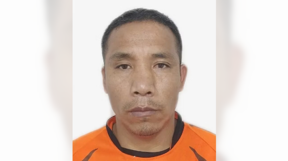 A man pictured against a white background. He is middle aged with cropped black hair and wears an orange and black top.