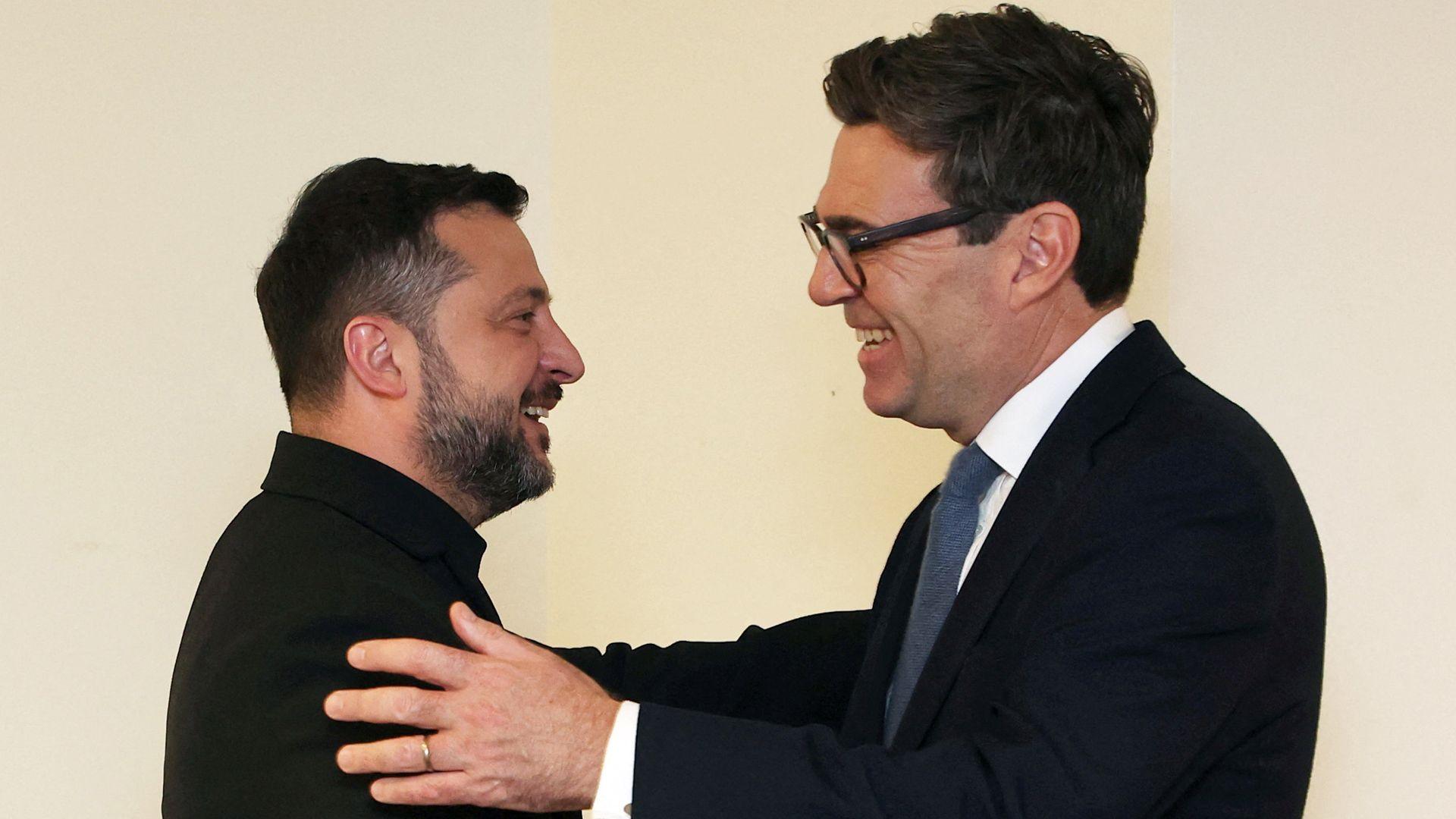 A head and shoulders shot of Zelensky on the left, who has a close-cropped beard and is wearing a black top. On the right is a shot of Burnham, wearing a navy suit and white shirt with a tie. The pair are facing each other and smiling, and Burnham has his hand on Zelensky's arm.