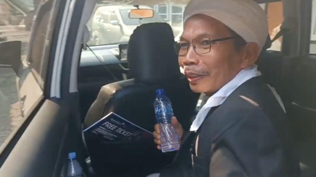A man, holding a water bottle, is getting out of the back seat of a car.