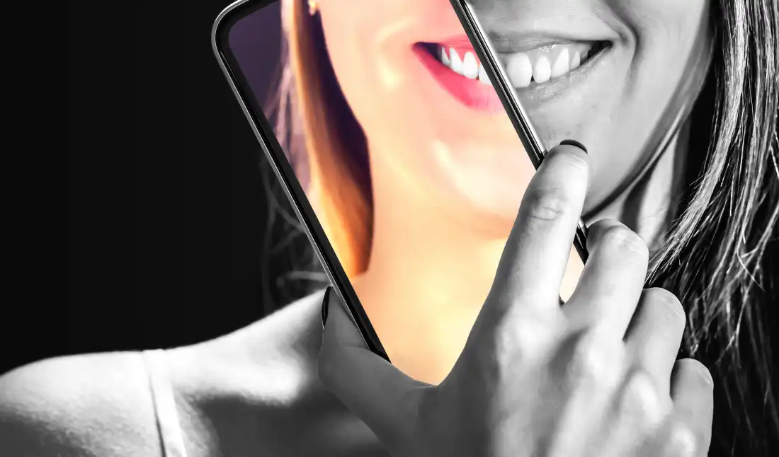 A photo illustration of a phone (in color) in front of person's face, which is in black and white.